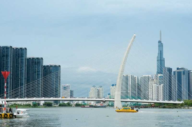 Cầu Ba Son (cầu Thủ Thiêm 2) với trụ tháp cong bắc qua sông Sài Gòn, phía sau là tháp Landmark 81 và các tòa cao tầng, một chiếc tàu vàng trên sông
