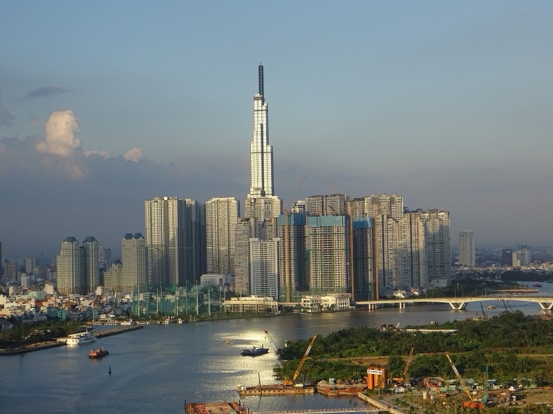 Tháp Landmark 81 dưới nắng chiều bên sông Sài Gòn, phía trước là bờ sông đang thi công với cần cẩu và sà lan