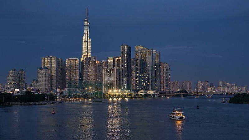 Tháp Landmark 81 và các tòa cao tầng ven sông Sài Gòn lúc trời chạng vạng, một chiếc tàu nhỏ đang chạy trên sông