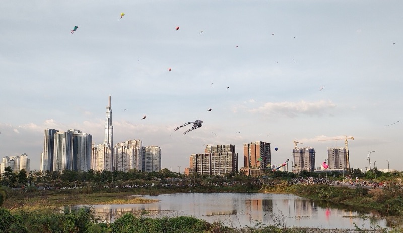 Nhiều cánh diều bay trên bãi đất trống ven hồ nước ở Thủ Thiêm, phía xa là tháp Landmark 81 và các tòa chung cư